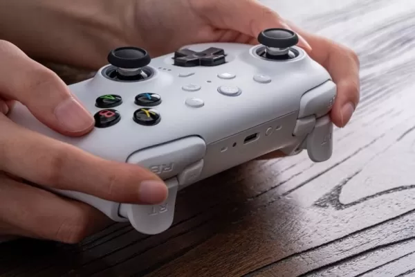 Ein Bild von einer Person, die einen weißen Spielcontroller auf einem Holzschreibtisch hält